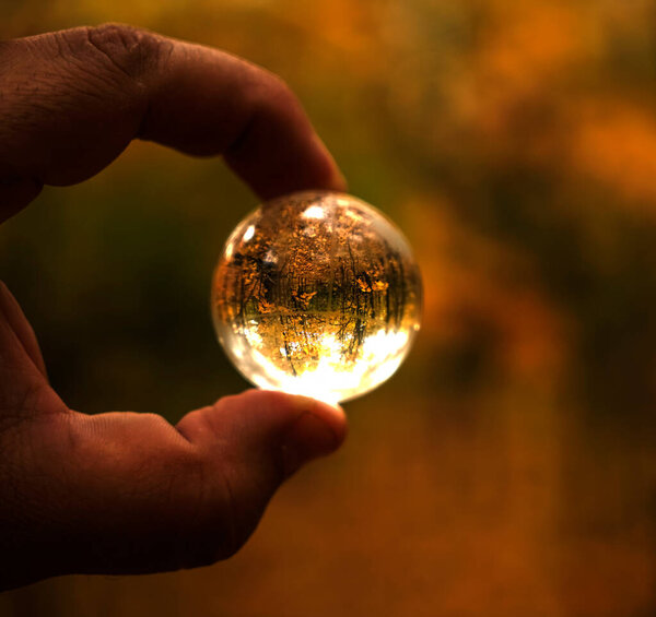 A hand holding a lens ball in which autumn park reflects. Lens balls made of glass. transparent globe map