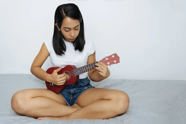 Jovem Latino Mulher Jogar Ukulele Sentado Cama Parede Branca — Fotografia de Stock