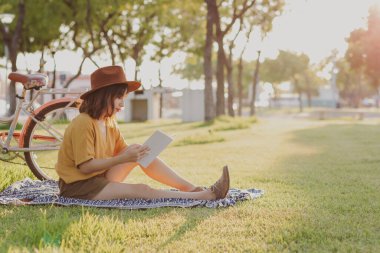 Arka planda seçici bir odak bisikletinde şapka okuyan genç bir kadın.
