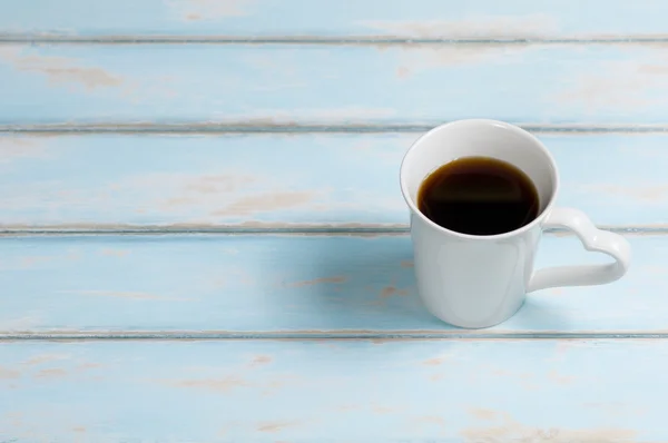 Black coffee in cup with heart handle on sky blue color wood. Royalty Free Stock Images