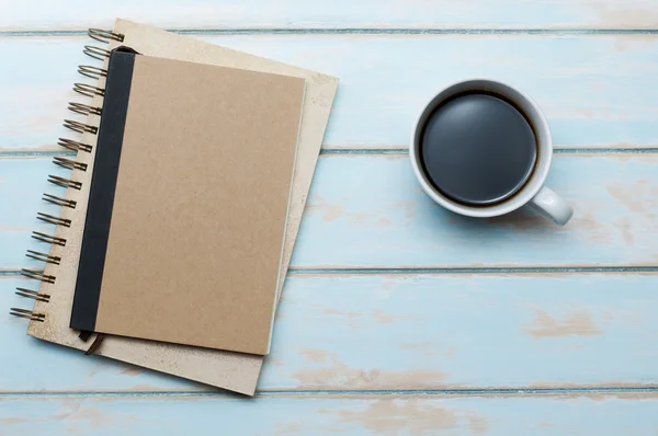 Černá káva s Poznámkový blok a deník na dřevěné podlaze modrá obloha. — Stock fotografie