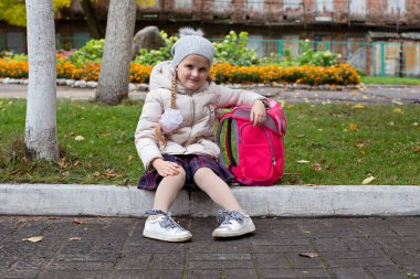 Sırt çantası kaldırımda oturan neşeli bir öğrenci.