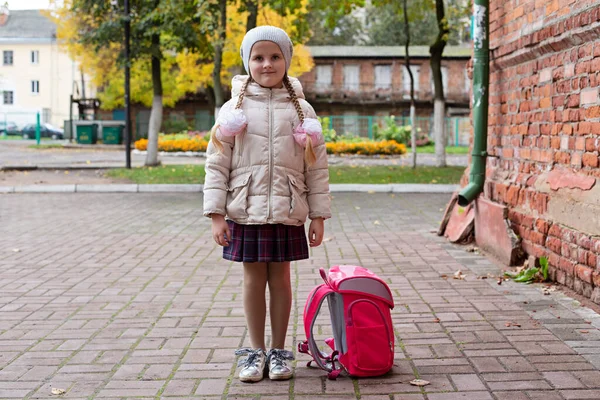 Дівчинка-школярка стоїть на вулиці з рюкзаком. Дитину чекають підібрати після школи — стокове фото