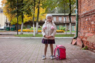 Okul üniforması içinde sokakta duran sırt çantalı bir kız öğrenci..