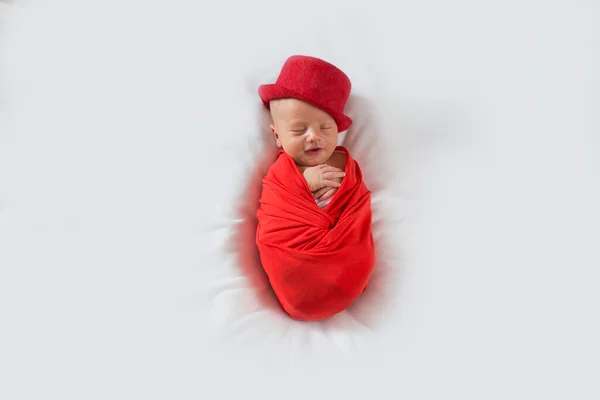 Bebé recién nacido con un traje rojo y sombrero sobre un fondo blanco. Niño recién nacido dormido con un sombrero rojo con una sonrisa en la cara. —  Fotos de Stock