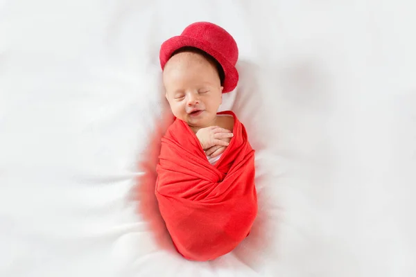 Sova nyfödd pojke i en röd hög hatt med ett leende på läpparna. Vackert foto av en nyfödd i herrkostym — Stockfoto