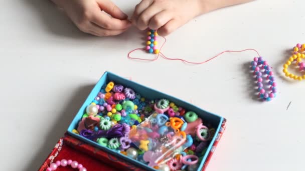 Маленька дівчинка нанизує намистини на нитку, щоб створити браслет — стокове відео