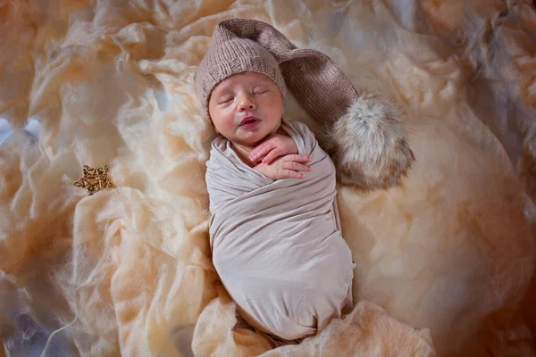Bayi yang baru lahir sedang tidur. Anak kecil yang tidur memakai jas dengan sebuah pompom dan tanda bintang Stok Foto Bebas Royalti