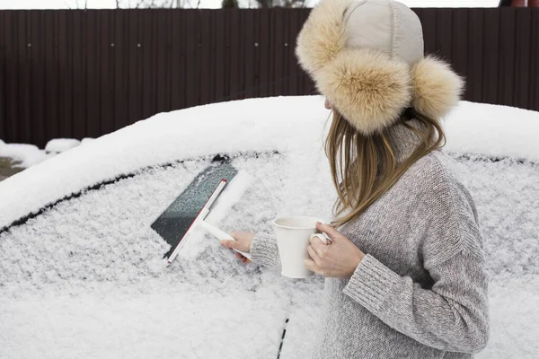 Foto eines Mädchens, das die Scheibe eines Autos vom Schnee reinigt. lizenzfreie Stockbilder