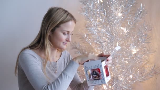 En ung attraktiv europeisk kvinna sitter hemma och packar upp en julbal. Väntar och förberedelser för semestern — Stockvideo