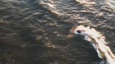 Gün batımında skuter üzerinde uçan insan görüntüsü dalgaların üzerinde atlıyor. 