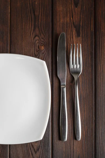 Empty plate, fork and knife on dark wood background — Stock Photo, Image