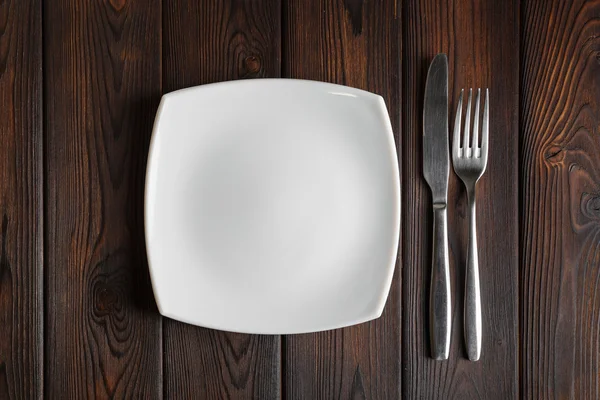 Empty plate, fork and knife on the dark wood background — Stock Photo, Image