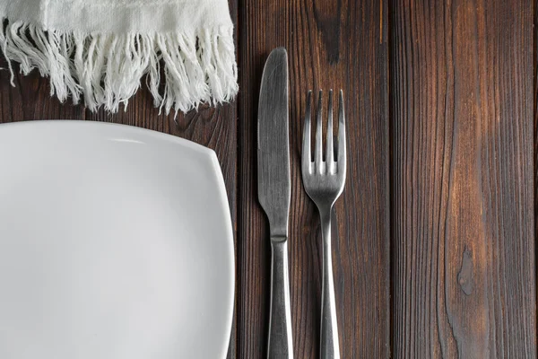 Empty plate, fork and knife on dark wood background — Stock Photo, Image