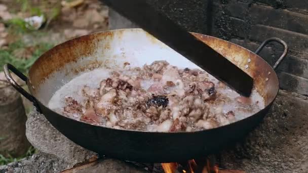 Размешивание обжаренных кусочков свинины внутри вока деревянной палкой над открытым огнем — стоковое видео