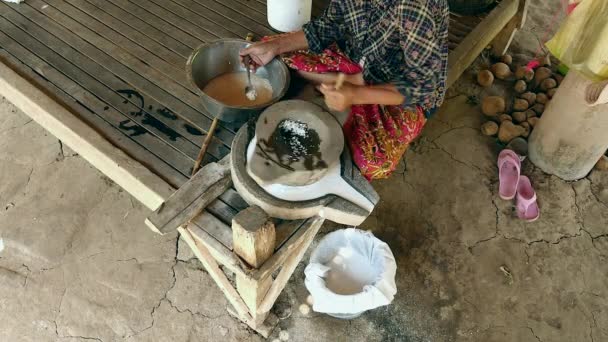 Woman sat cross-legged using hand-turned millstone to grind wet rice for making soaked rice flour — Stock Video