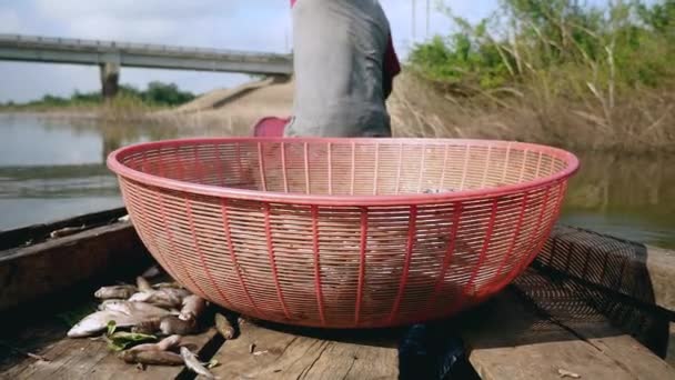 Close-up on a plastic fishing basket in a dugout canoe; Fisher sitting in the bow rowing the boat on a lake — Stock Video