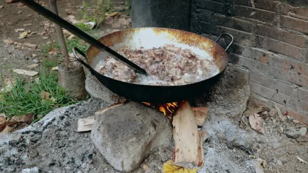 Roeren van Frituur stukjes varkensvlees in een wok met behulp van een houten stok over open vuur — Stockvideo