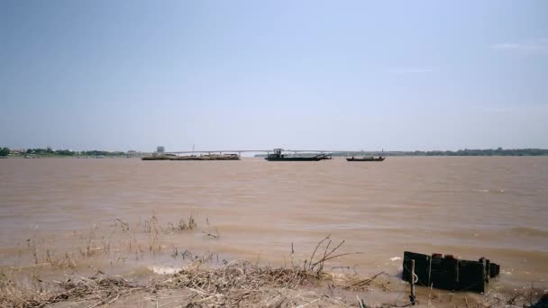 Vista de distancia de una barcaza está tirando detrás de un gran montón de postes de bambú hacia la orilla del río — Vídeo de stock