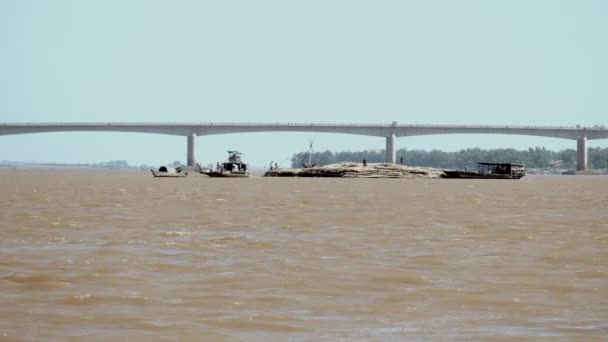 Barge tirant derrière un grand tas de poteaux de bambou vers la rive — Video