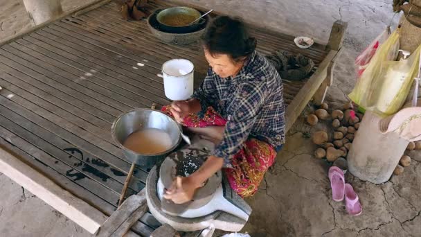 Mujer se sentó con las piernas cruzadas usando piedra de molino vuelta a mano para moler el arroz húmedo para hacer harina de arroz empapada — Vídeos de Stock