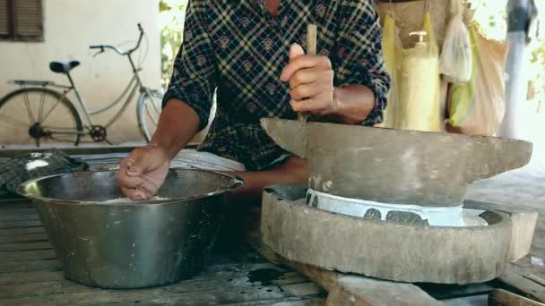 Woman sat cross-legged using hand-turned millstone to grind wet rice for making soaked rice flour — Stock Video