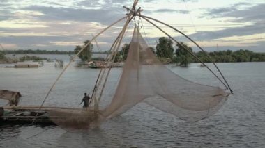 Fisher sabah erken saatlerde çin balık ağı yakalanan balıkları almak için bir el ağı kullanarak