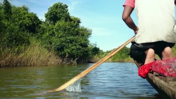 Fisher remando desde el lado de proa una canoa dugout en un lago bajo el cielo despejado — Vídeos de Stock