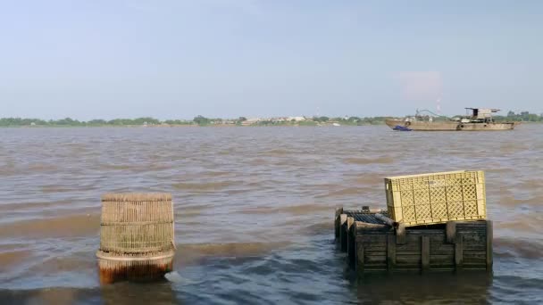 Captures de poisson conservées dans des caisses à poisson en bois et des conteneurs en plastique sur le bord de la rivière ; vieux bateau de dragage descendant la rivière comme toile de fond — Video