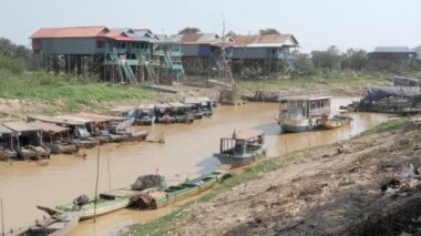 Kurak mevsimde nehirde yüzen bir köyden geçen uzun kuyruklu bir balıkçı teknesinin yan görüntüsü.
