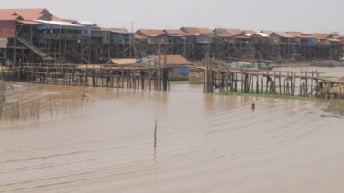 Küçük bir köprünün altından geçen uzun kuyruklu balıkçı tekneleri. Nehir kıyıları boyunca yüzen köy..