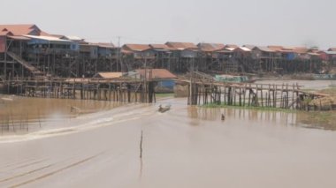 Küçük bir köprünün altından geçen uzun kuyruklu balıkçı tekneleri. Nehir kıyıları boyunca yüzen köy..