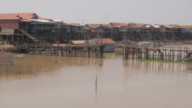 Küçük bir köprünün altından geçen uzun kuyruklu balıkçı tekneleri. Arkaplan olarak yüzen köy