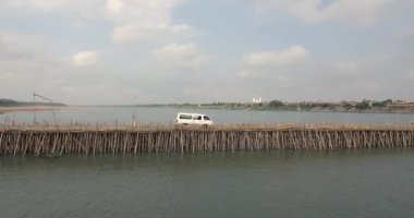 Nehir üzerinden bambu köprüsünü geçen bir minivanın hava görüntüsü.