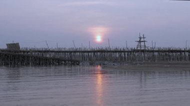 Motosikletler güneş doğarken Mekong nehri üzerindeki bambu bir köprüde birbirinin yanından geçiyor (zaman aşımı)) 