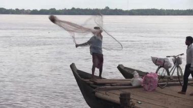 Balıkçı, ahşap iskeleye demirlemiş bir tekneden nehre ağ atıyor.