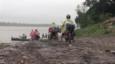 Motosikletler iskeleye ulaşmak için kırık bambu döşemeli çamurlu rıhtımlarda ilerliyorlar. Yağmurlu gün.