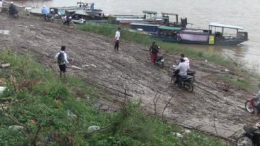 Motosikletleriyle birlikte yağmurda çamurlu bir rıhtımda yürüyen feribot yolcuları.