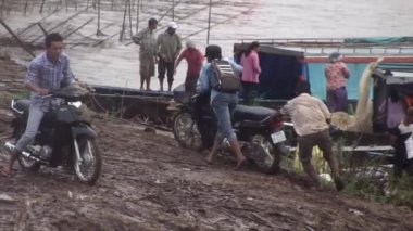 Adam yağmurda çamurlu rıhtım yolunda motosiklet sürüyor.