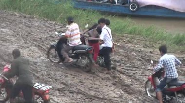 Limandan kasabaya giden çamurlu bir patikada motosikletleriyle birlikte yürüyen feribot yolcuları.