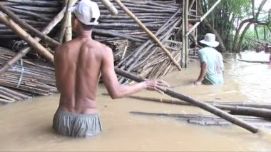 Su basmış bir depoya bambu direkleri yükleyen işçilere yakın durun.