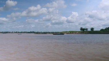 Bulutlu gökyüzünün altında (hareket halindeki bir tekneden çekilen) nehri geçen yolcularla birlikte feribot.)