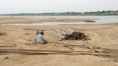 Kumsalda bambu sapı kesen iki kadın.