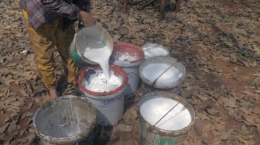 close up of a farmer pouring harvested latex in a  bucket using a plastic strainer