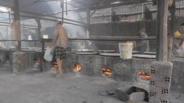 Phnom Penh - Kamboçya - 14- 08- 2021; deri tofu yapmak için bakır tavada soya sütü kaynatmak. Sıvıyı döken işçiler yemek pişirme tavasının altına odun koyuyor. 