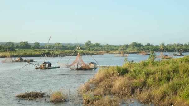 Houseboats with chinese fishing nets on river and fisherman using a dip net with chinese net in the foreground — Stock Video