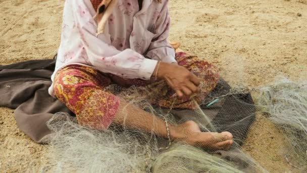 Close-up van een vrouw zitten op de oever te herstellen van een visnet met de hand — Stockvideo