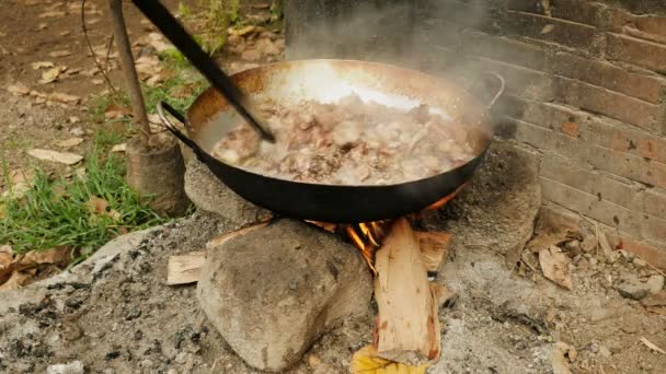 Τηγάνισμα χοιρινό μέσα σε ένα γουόκ χρησιμοποιώντας ένα ξύλινο ραβδί πάνω από ανοιχτή φωτιά ανακατεύοντας — Αρχείο Βίντεο