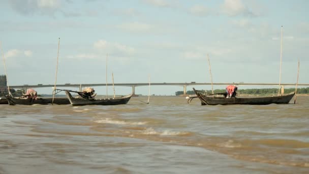 การประมงขุดเรือแคนูผูกติดกับเสาไม้ไผ่ติดอยู่ในแม่น้ําลมและชาวประมงดึงตาข่ายผ่านน้ําเป็นพื้นหลัง — วีดีโอสต็อก