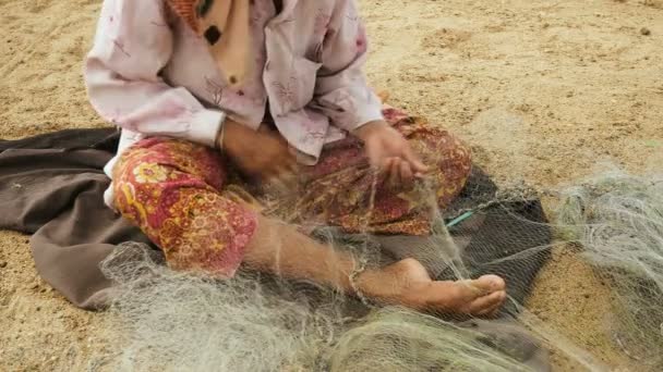 Close-up on a woman sitting down on the riverbank to mend a fishing net by hand — Stock Video